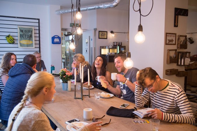 Guests at Wombat's City Hostel London's café share laughs and stories under the soft glow of pendant lights, surrounded by chic decor and the buzz of hostel life."
