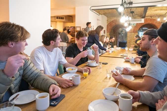A lively group of travelers laughing and eating together at a long communal table in Wombat's City Hostel London