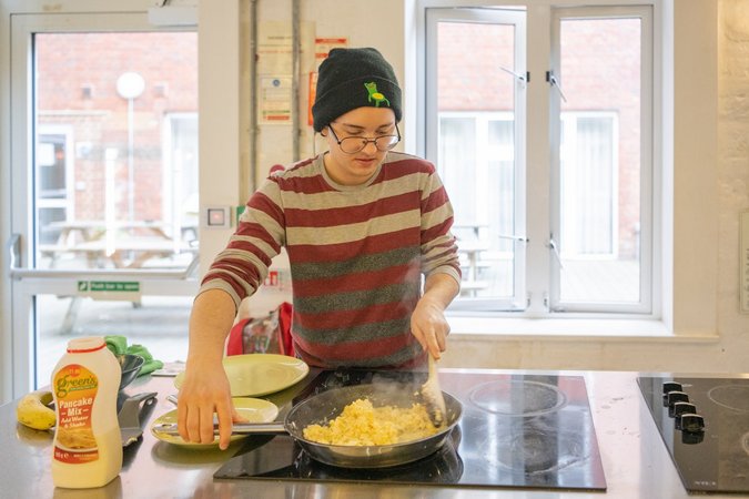 A guest cheerfully prepares food in the bright and fully equipped kitchen of Wombat's City Hostel London
