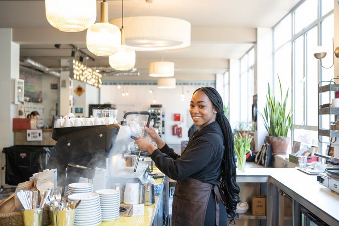 A barista at Wombat's City Hostel London joyfully prepares a drink